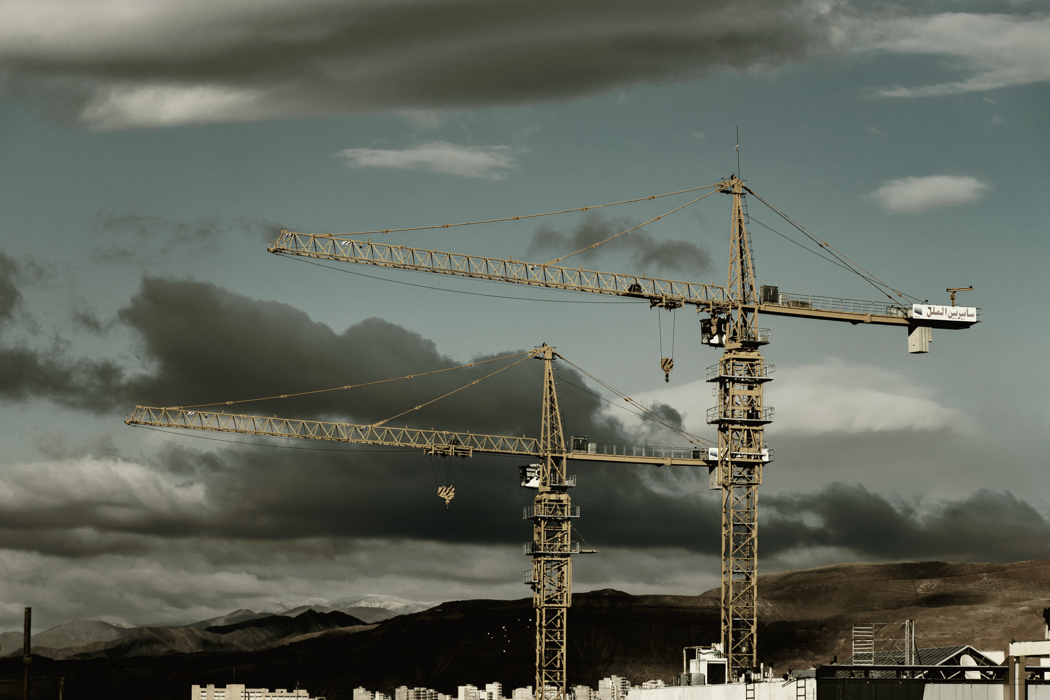 Two tower cranes crossing above an unfinished concrete structure.