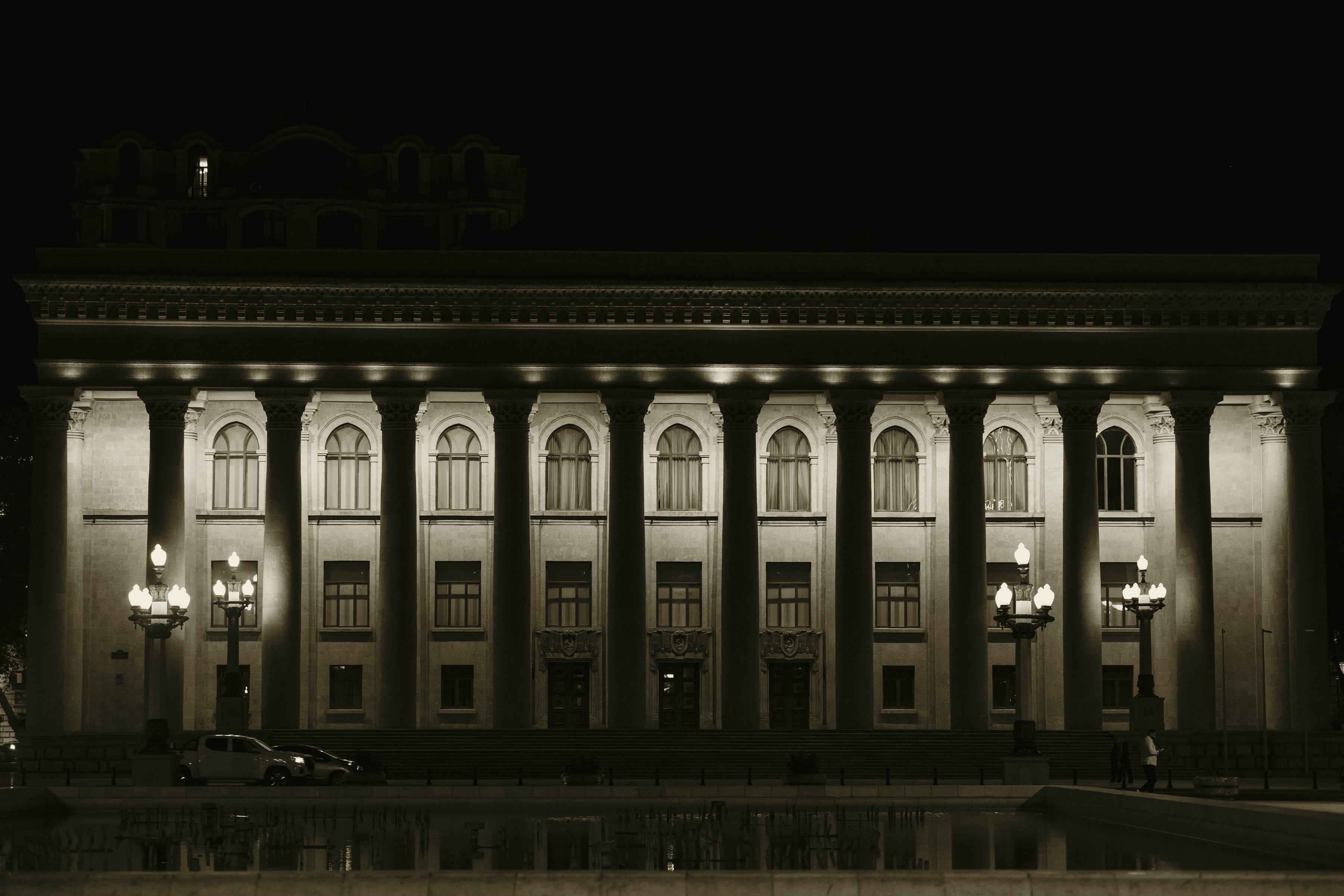 A monumental colonnade lit after dark, a single figure small against it.