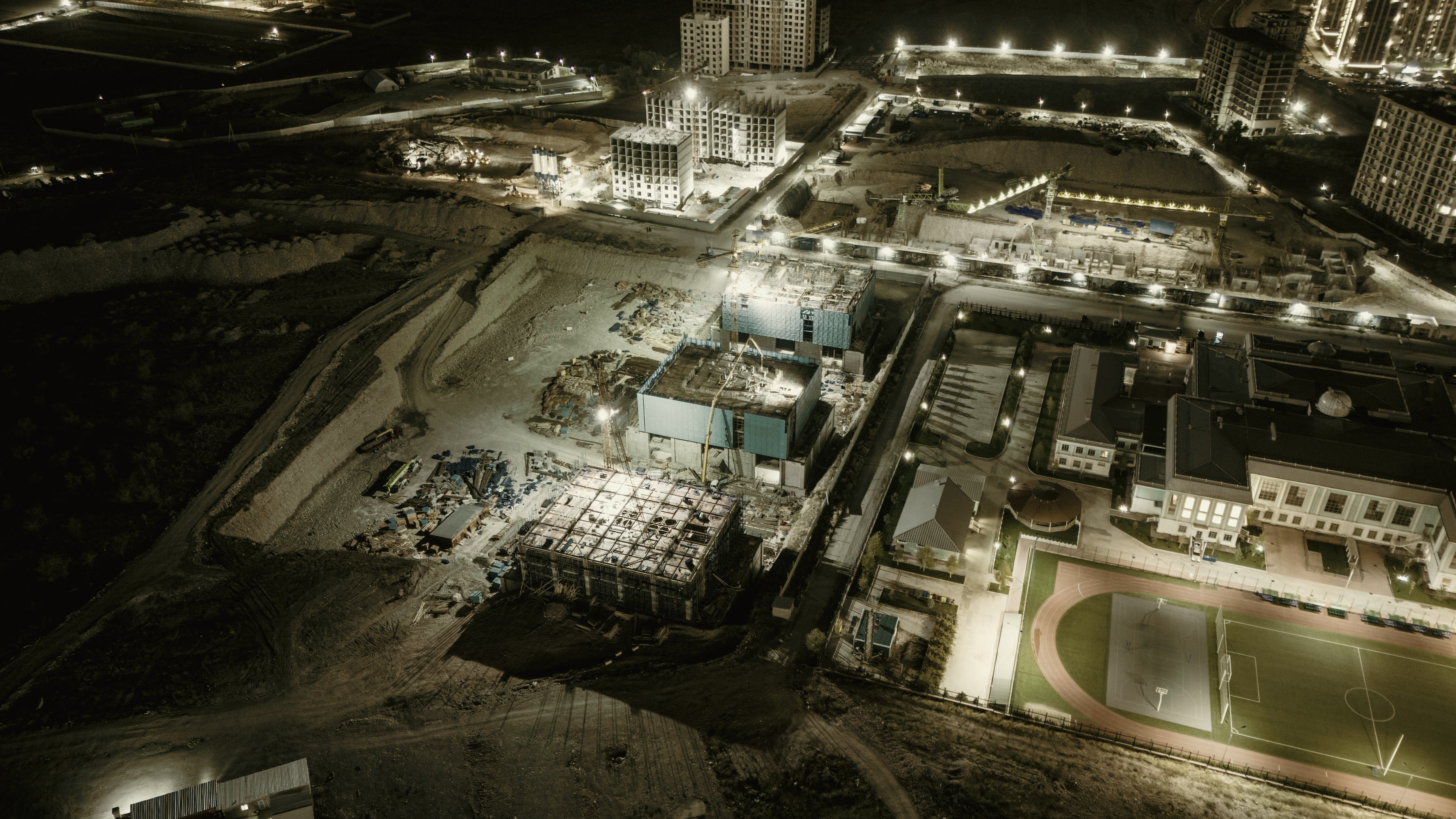 A construction site at night seen from above, floodlit and still working.