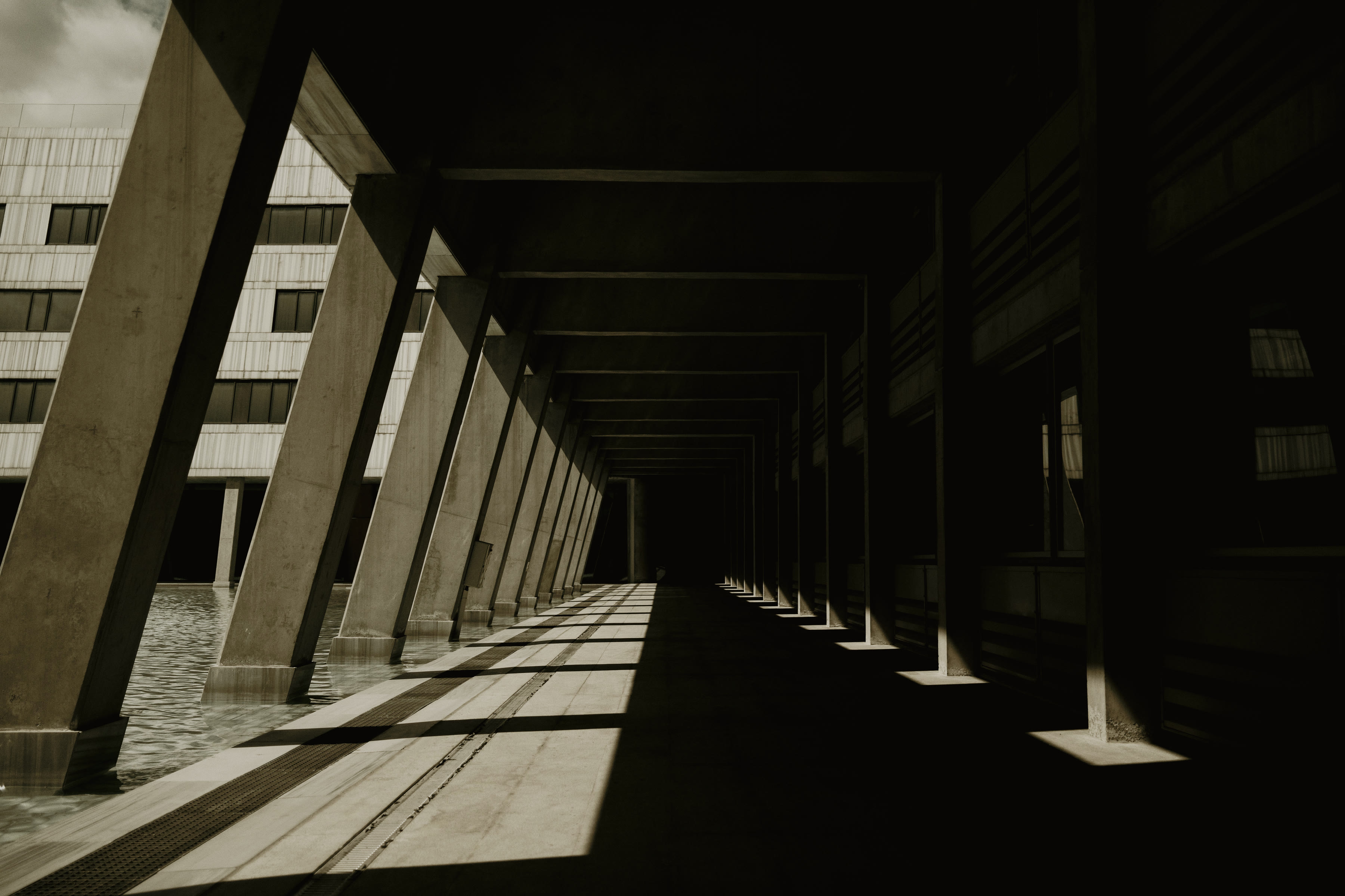 A concrete colonnade in hard shadow, its bays receding into darkness.