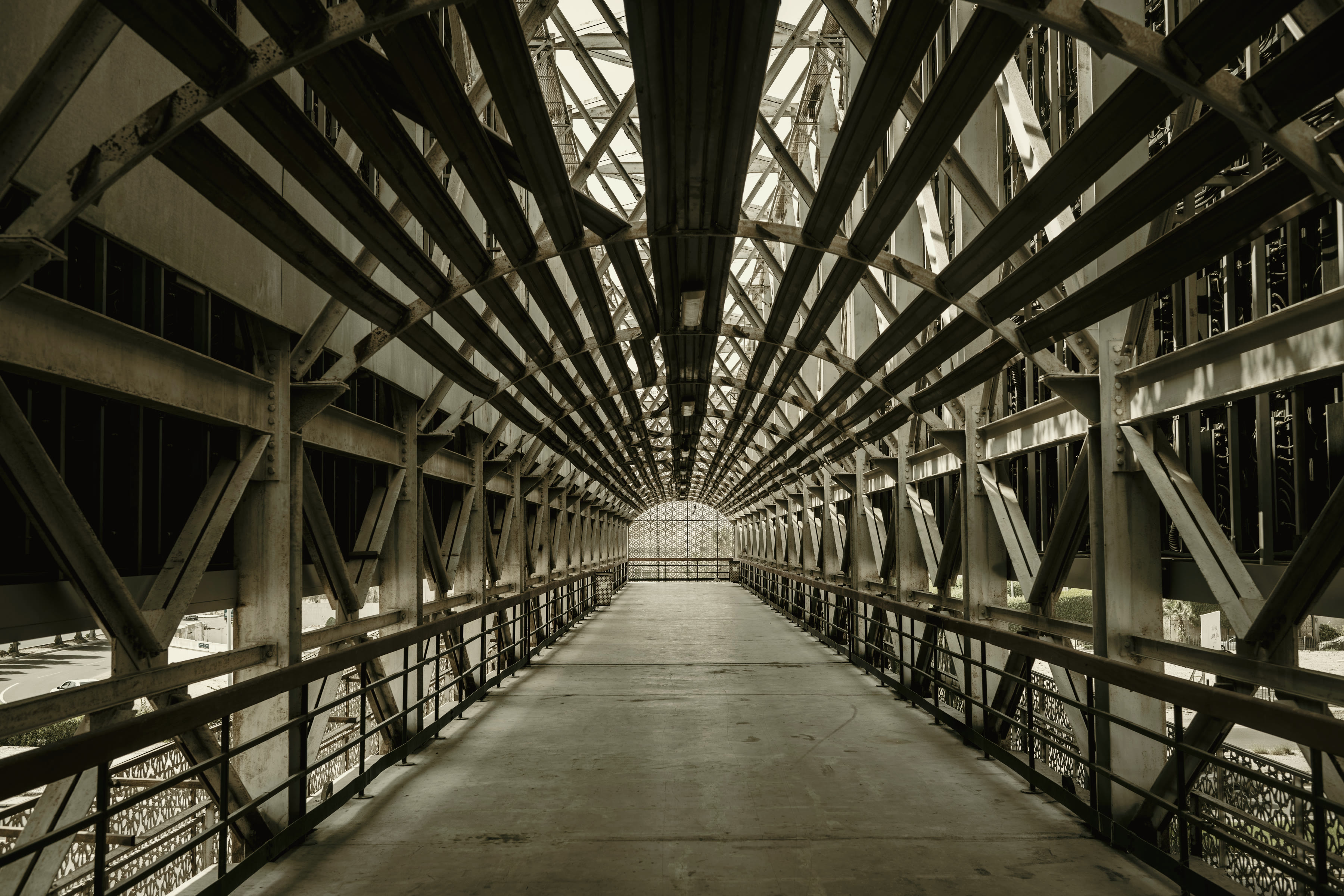 Inside a steel truss walkway, its members repeating away down the span.